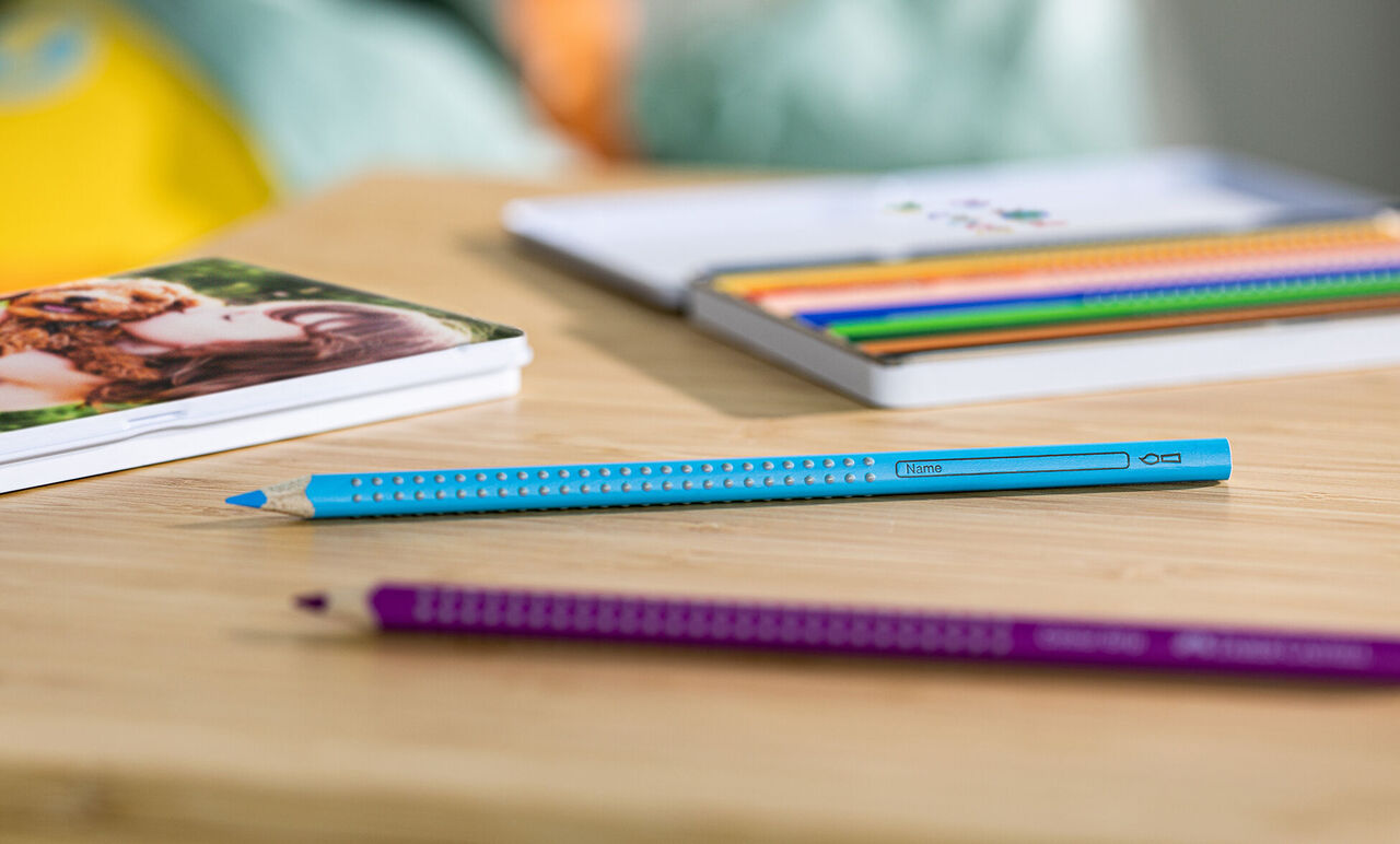 Des crayons colorés sur une table en bois avec un livre photo en arrière-plan.