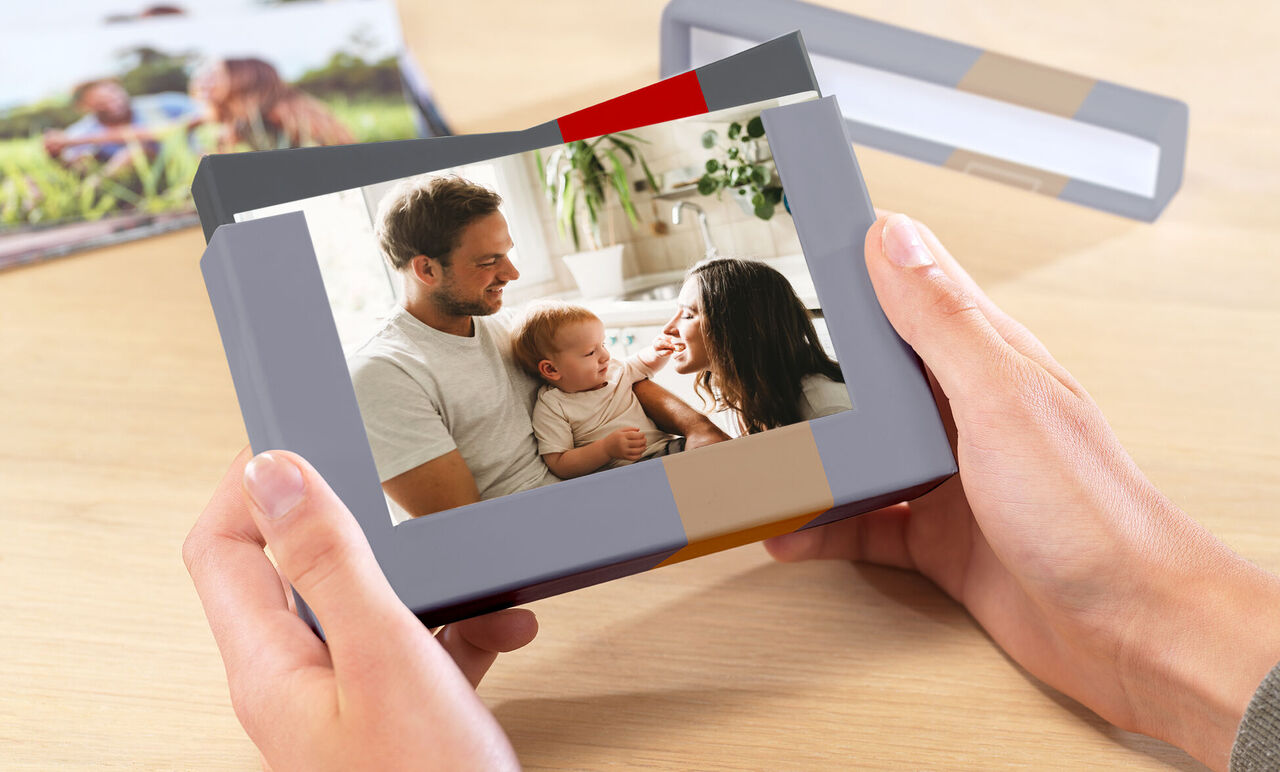 Une personne heureuse tient un album photo soigneusement conçu. La couverture montre une famille s'amusant.