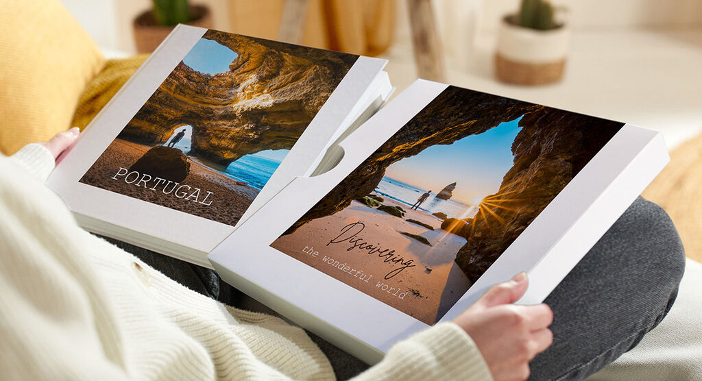 Deux livres photo CEWE avec des photos de vacances tenus par une personne.