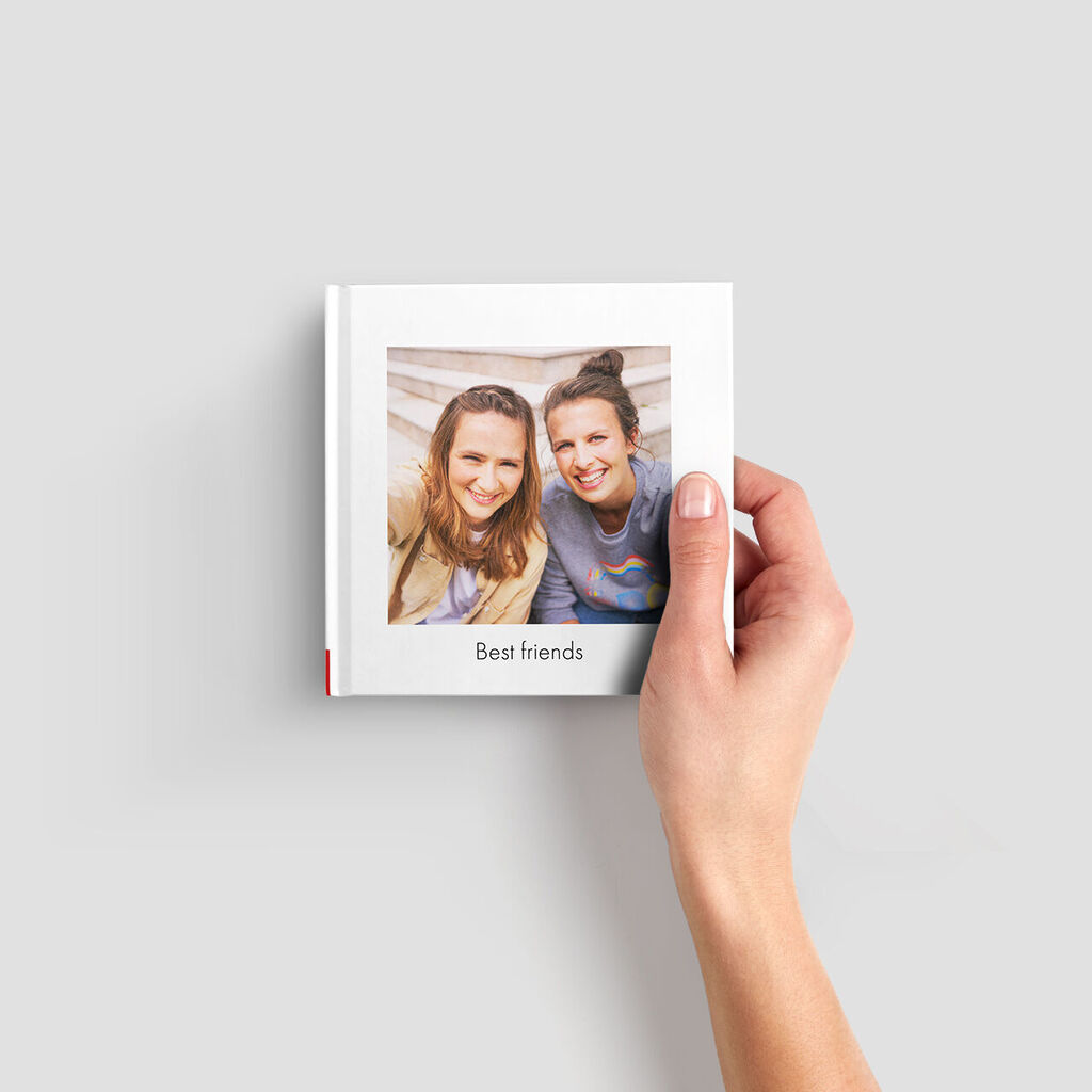 Une main tient un album photo intitulé 'Meilleurs amis' avec une fenêtre pour une photo personnelle.