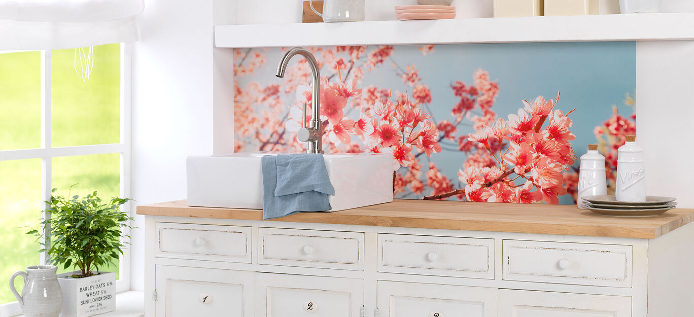 Cuisine lumineuse avec un évier blanc, à côté une serviette et un mur de fleurs de cerisier.