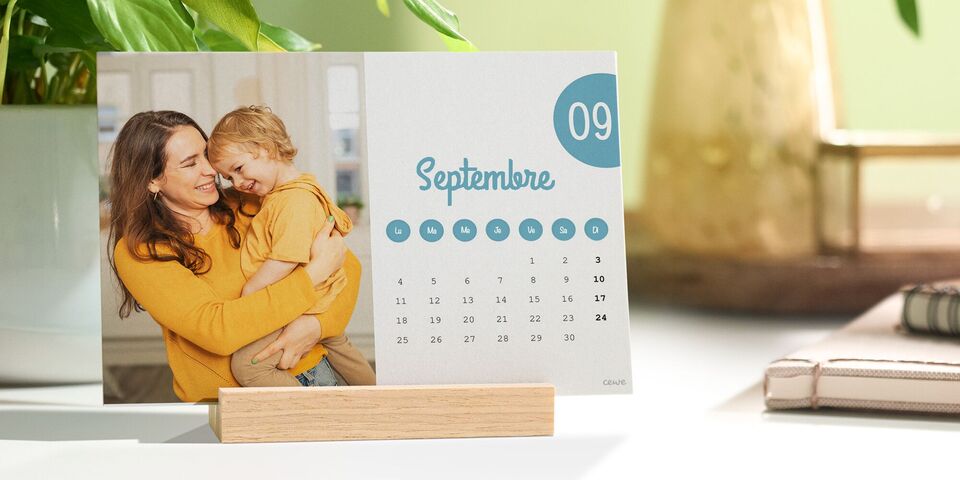 Un calendrier de bureau avec une photo d'une mère et son enfant est posé sur un bureau dans un support en bois.