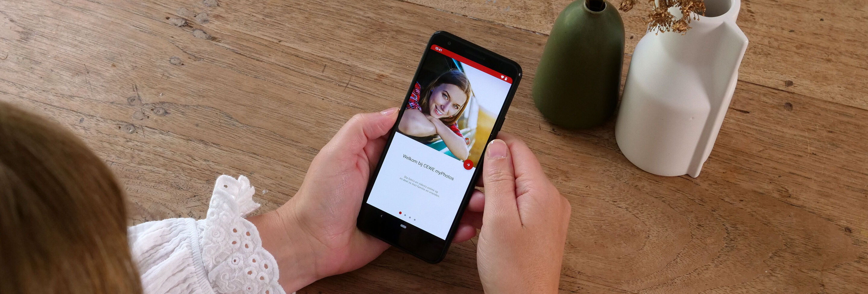 Une personne regarde une image sur son smartphone, avec deux vases sur la table.