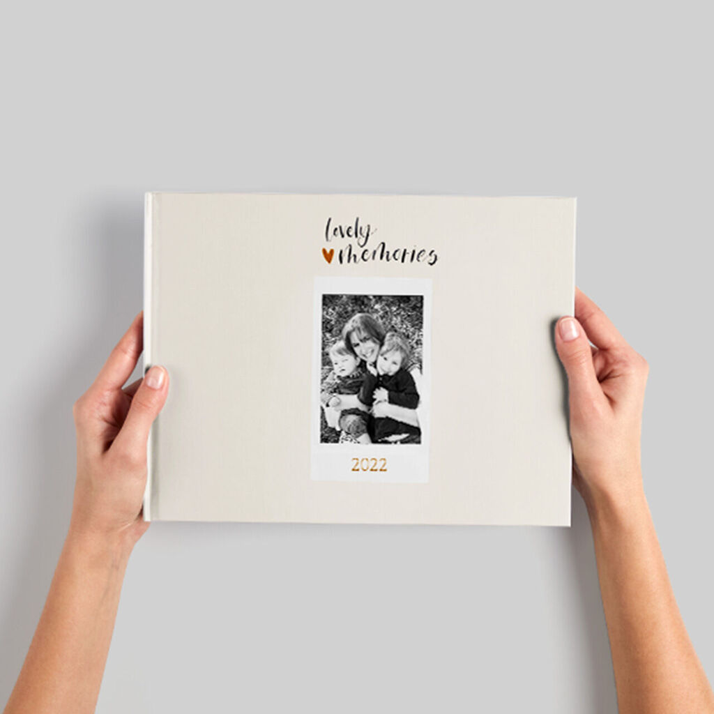 Deux mains tenant un livre photo soigneusement conçu avec une photo instantanée de deux enfants.