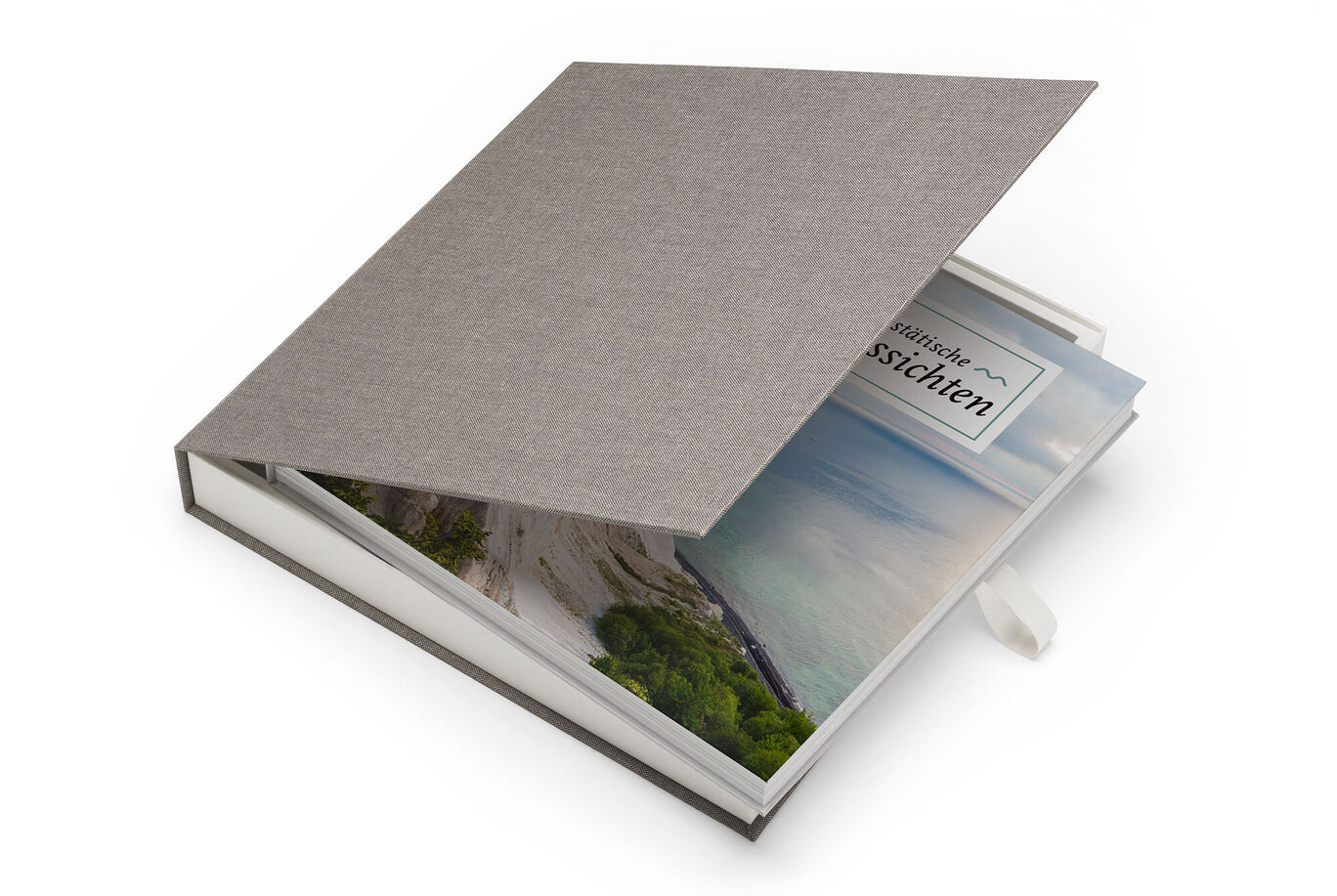 Un élégant CEWE FOTOBUCH avec une couverture en tissu grise et une fenêtre montrant un paysage coloré.