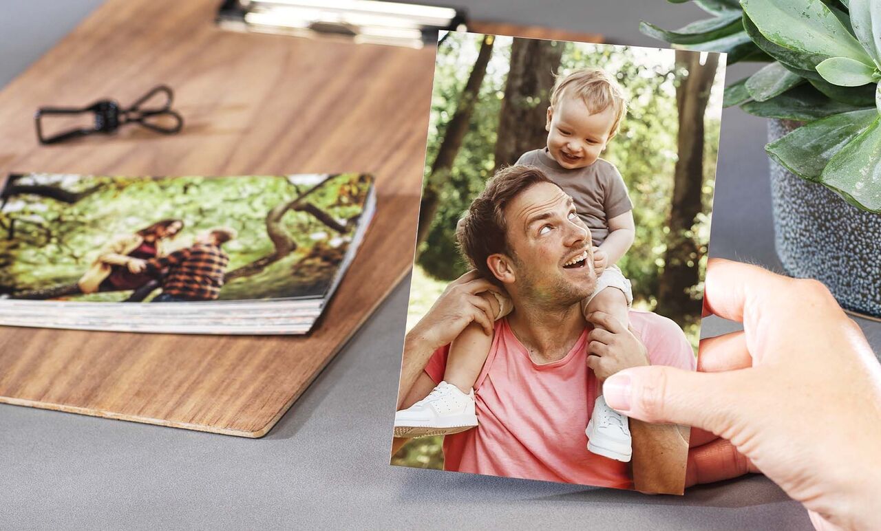 Une main tient une photo d'un père portant son enfant sur ses épaules. En arrière-plan, d'autres photos sur une table.