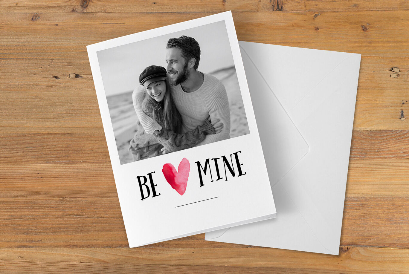 Un couple s'enlace souriant devant un fond clair. Sur la carte, "BE MINE" en grandes lettres.