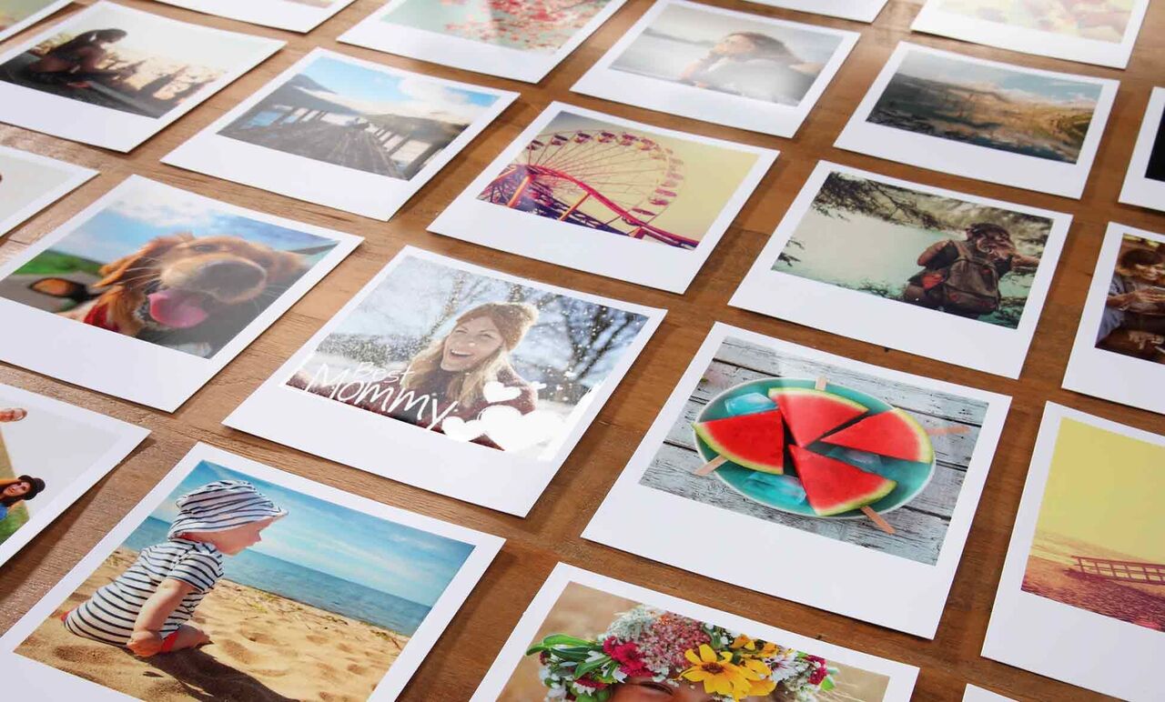 Divers tirages photos sont posés sur une table en bois. Les images montrent des gens heureux et de beaux moments.