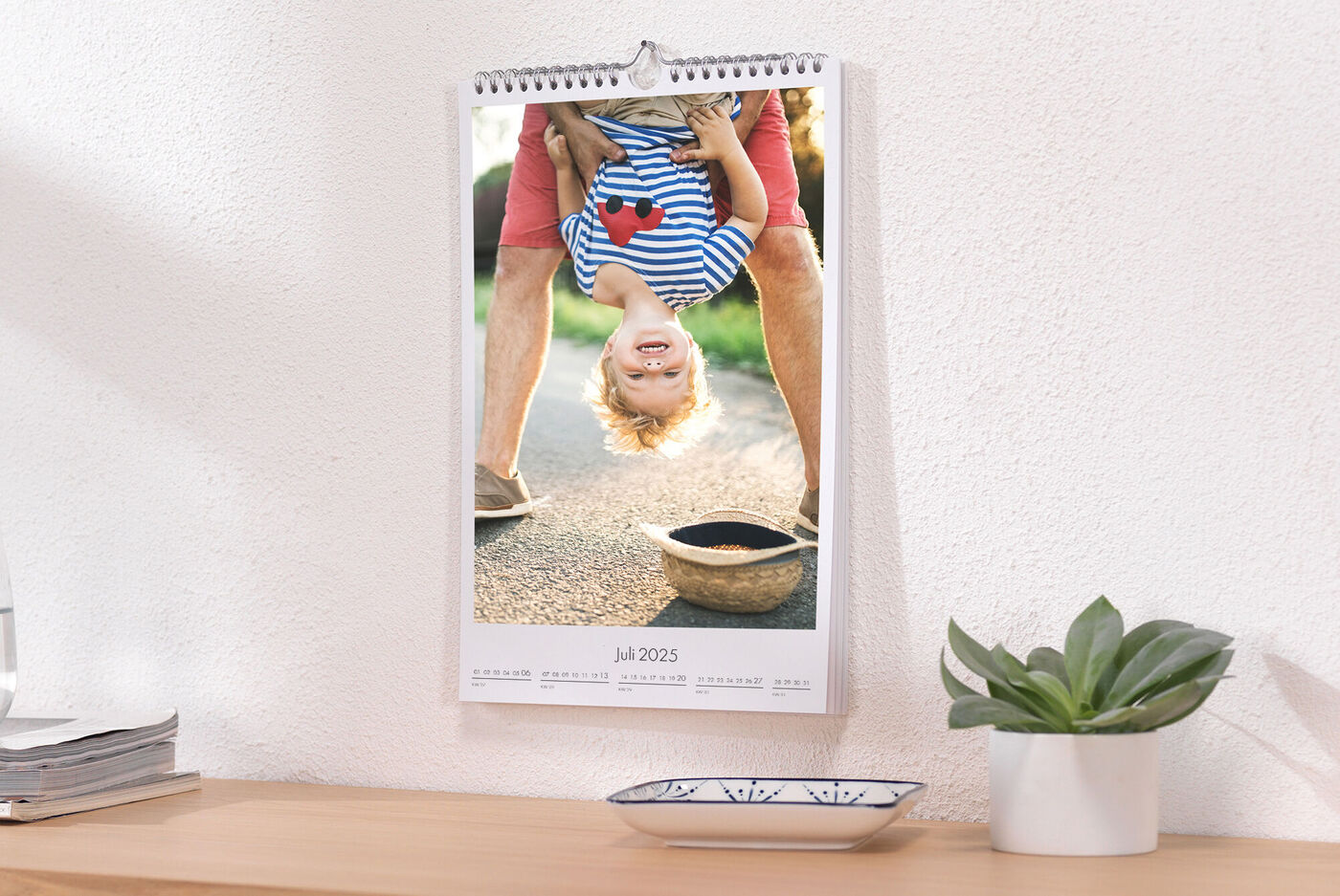Un enfant suspendu la tête en bas à une table. Un sourire joyeux sur son visage montre amusement et joie de vivre. Le calendrier est accroché au-dessus d'une table en bois.