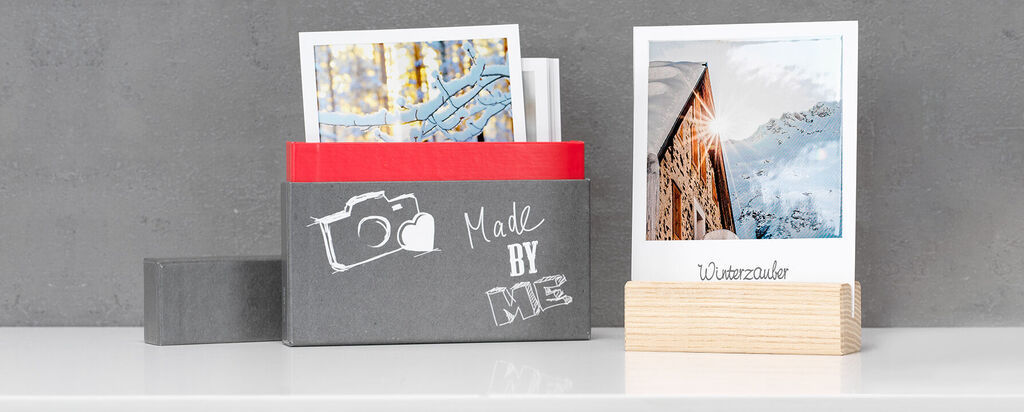 Boîte noire avec des photographies sur une table blanche, fond gris.