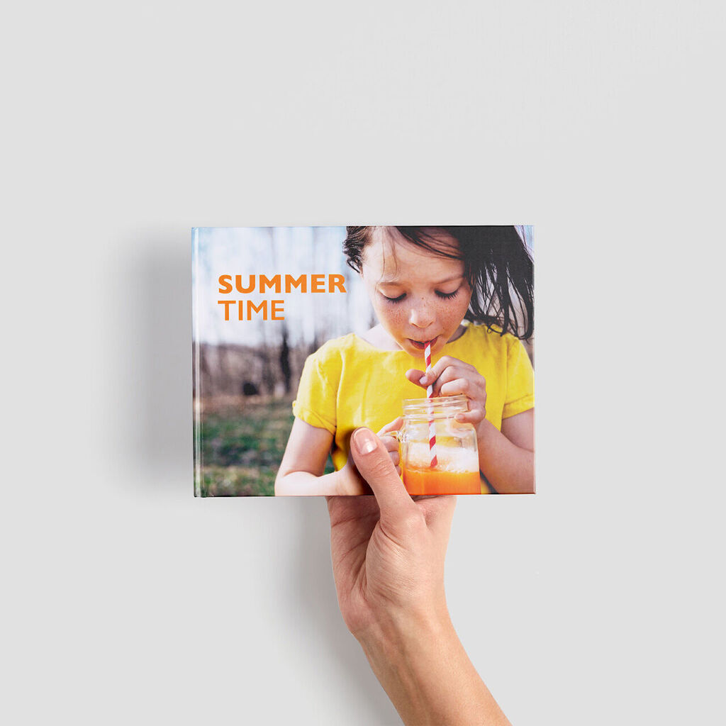 Une personne tient un album CEWE intitulé 'Summer Time' dans ses mains.