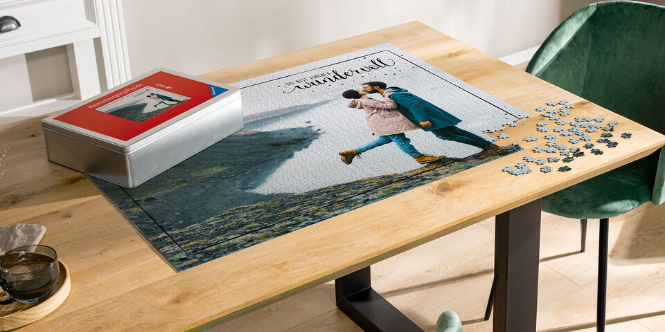 Un couple s'embrasse devant un paysage constitué de pièces de puzzle, avec une boîte de puzzle à côté.