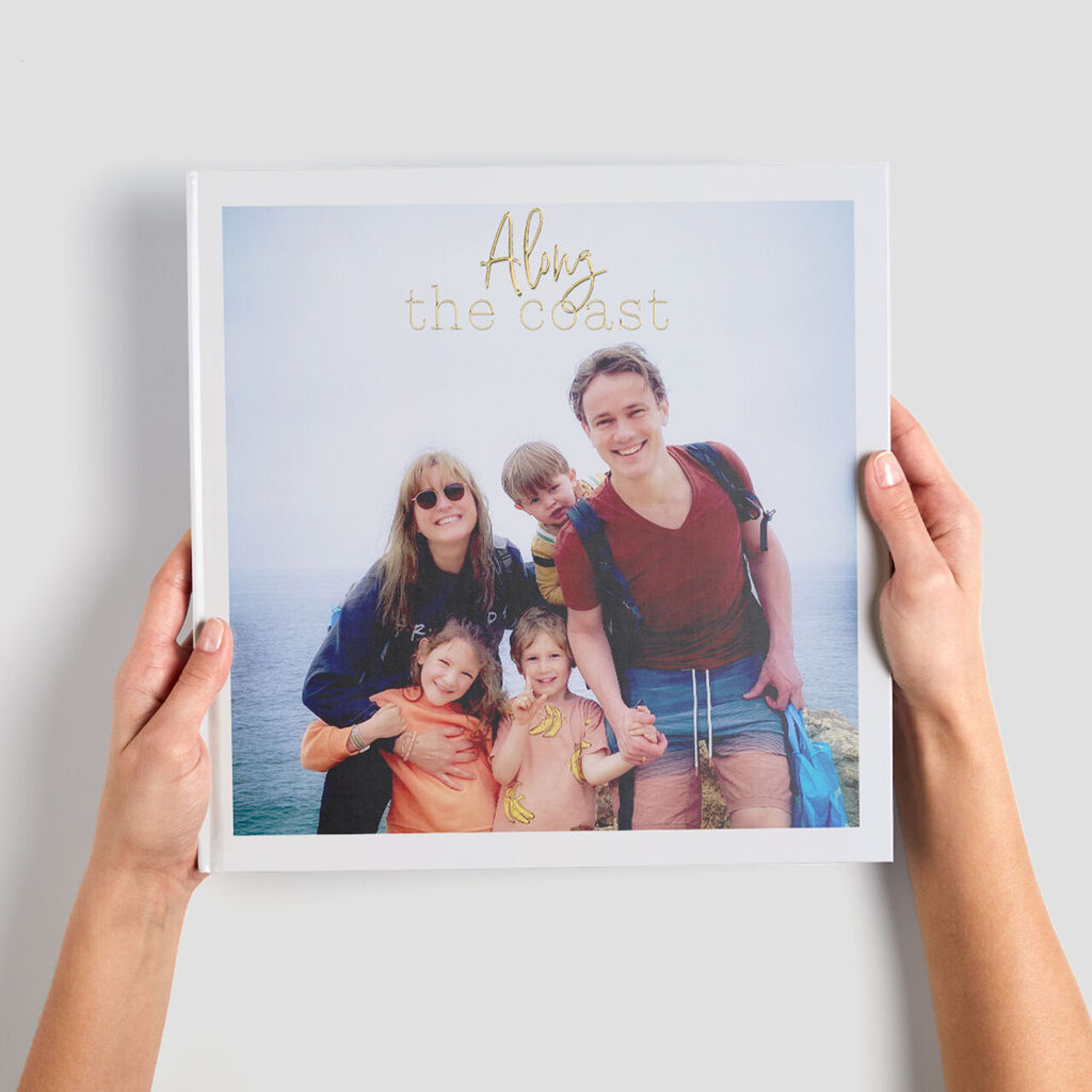 Une personne tient un livre photo CEWE intitulé 'Alys the coast' avec vue sur l'océan et le ciel.