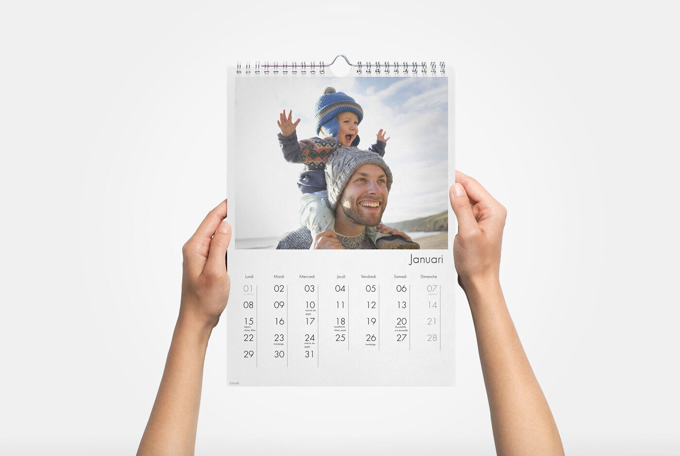 Een blij kind zit met plezier op een speelgoed en lacht naar de camera, terwijl het een kleurrijke hoed draagt. De kalender toont januari.