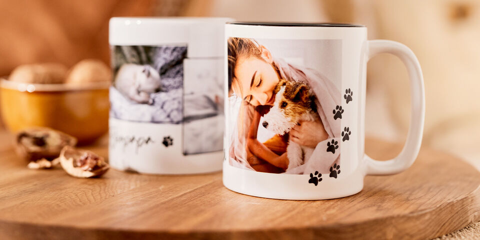 Een vrouw houdt een hond vast op een mok met pootafdrukken. Op de achtergrond staat een mok met een babyfoto.