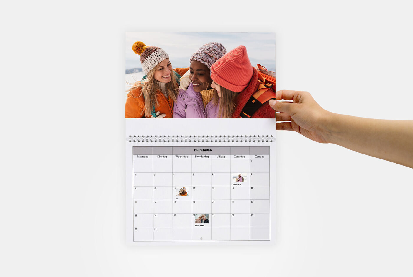 Drie meisjes met winterse mutsen bladeren door een CEWE fotokalender.